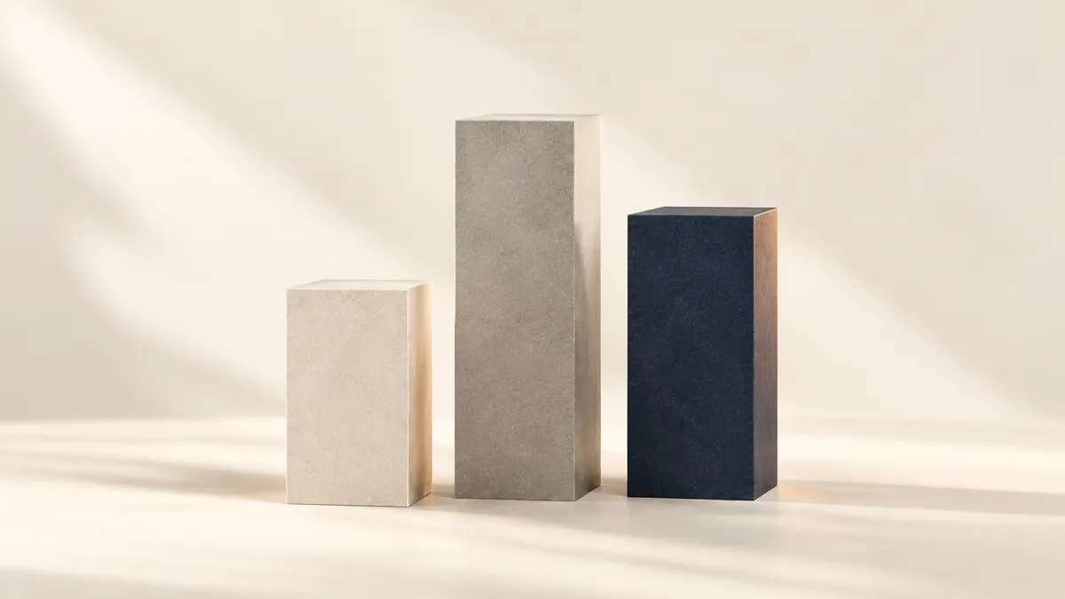 Three stone pillars of rising height in cream, grey and navy, standing side by side on a cream floor in soft daylight