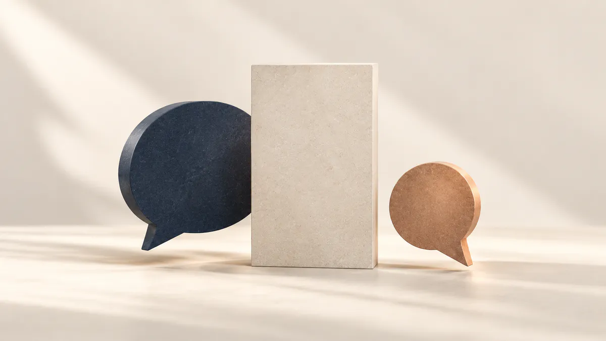 Navy stone speech bubble and smaller copper speech bubble on either side of a tall cream stone block in soft daylight